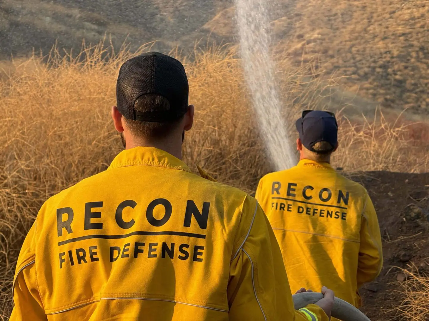 Two people in yellow jackets are standing next to a fire hydrant.